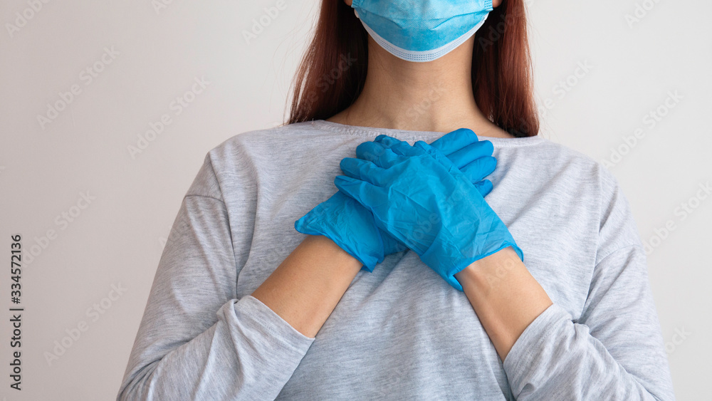 Fototapeta premium Woman with a surgical mask holding her hands in latex glove on her heart.