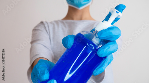 Disinfect your hands with antiseptic gel. Woman with a medical mask and hands in latex glove holding bottle of alcohol gel.