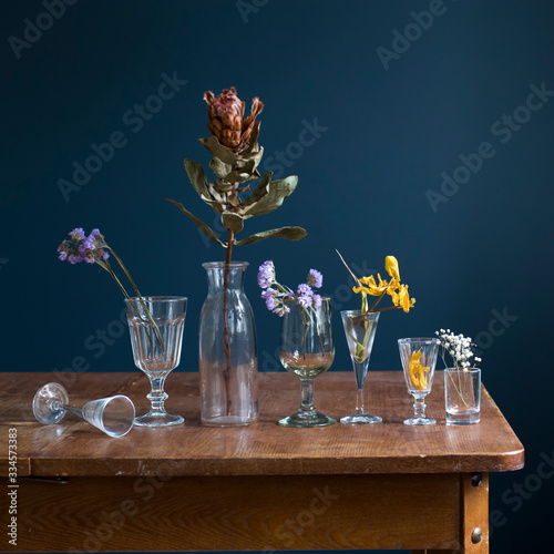 Obraz na plátně Dried flowers in glass glasses on a wooden table opposite a dark blue wall