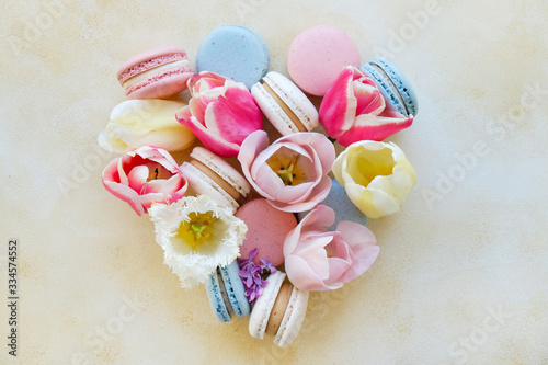 Feminine composition with traditional french macarons sweets and tender tulip flowers on yellow grunged concrete textured background. Top view, close up, copy space.