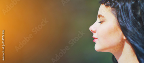 Beautiful young woman relaxing and enjoying sun at sunset. Beauty sunshine girl side profile portrait. Pretty happy woman enjoying summer outdoors. Positive emotion life success mind peace concept.