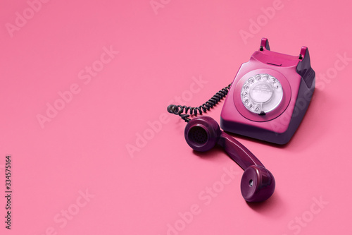 Pink vintage antique rotary phone with lifted handset receiver on a pink background with copy space and room for text with a right side composition.