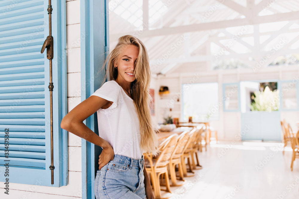 Attractive tanned lady with gorgeous smile posing in cafeteria early in morning. Photo of cute young woman in vintage outfit standing in restaurant Attractive tanned lady with gorgeous smile posing in cafeteria early in morning. Photo of cute young woman in vintage outfit standing in restaurant