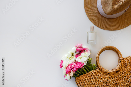 Conceptual image of woman's fashionable wicker bag with spring flowers. Colorful white and pink ranunculus bouquet over white background. Close up, copy space, cropped shot.