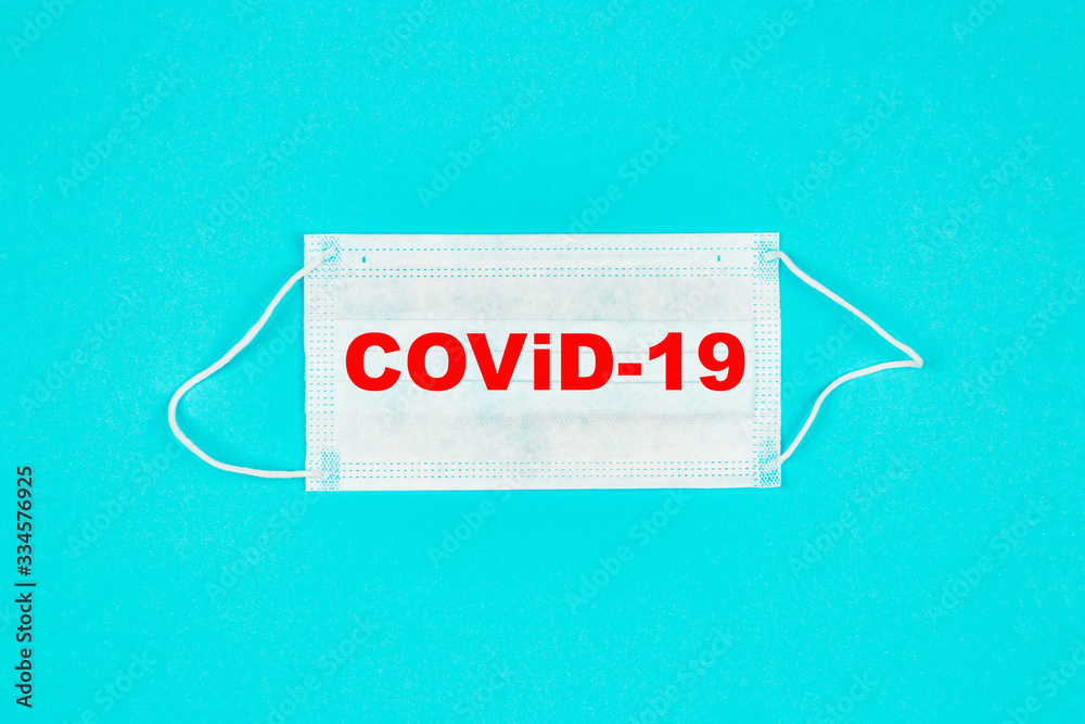 A close up of medical mask on blue background with text covid-19. Coronavirus protection. Copy paste for text. Top view. Flat lay.