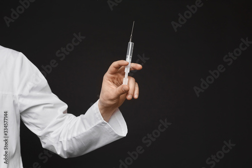 A medical syringe for injection with a vaccine in the male hand of doctor, isolated on black background with copy space. Concept of seasonal vaccination against viruses and illness