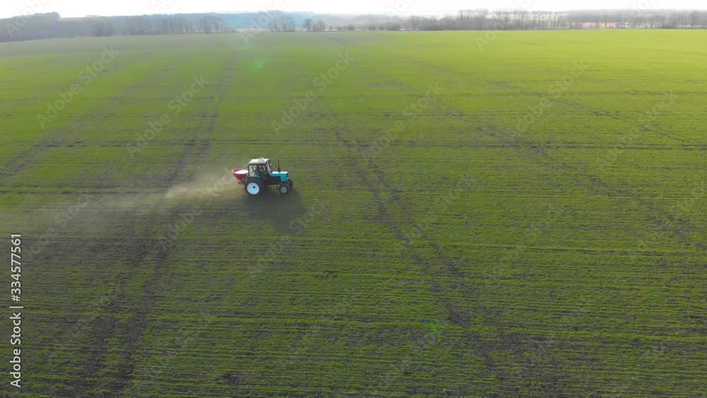 Tractor spreading artificial fertilizers in green field. Farmer fertilizing arable land with nitrogen and potassium fertilizer. Tractor spreading artificial fertilizers in green field. Farmer fertilizing arable land with nitrogen and potassium fertilizer.