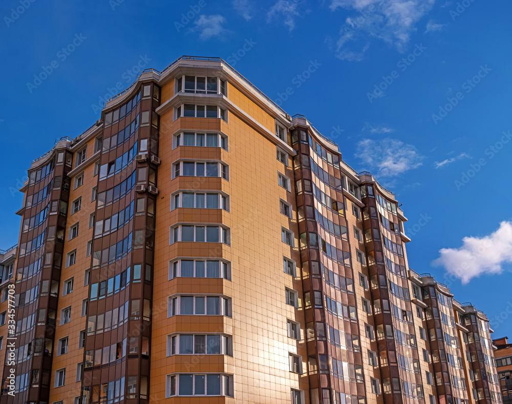 Modern residential building against the blue sky. The building has yellow walls and brown balconies