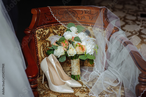 On the chair are shoes and a wedding bouquet. A veil is thrown on and the edge of the bride's dress is visible.
