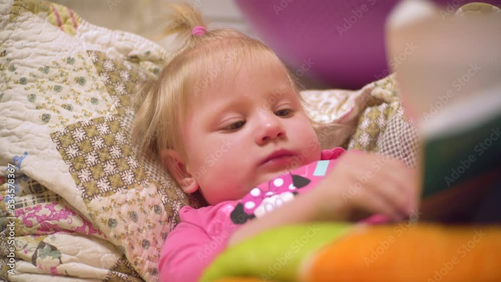a little girl with blond hair is lying on the bed reading a book a little girl with blond hair is lying on the bed reading a book