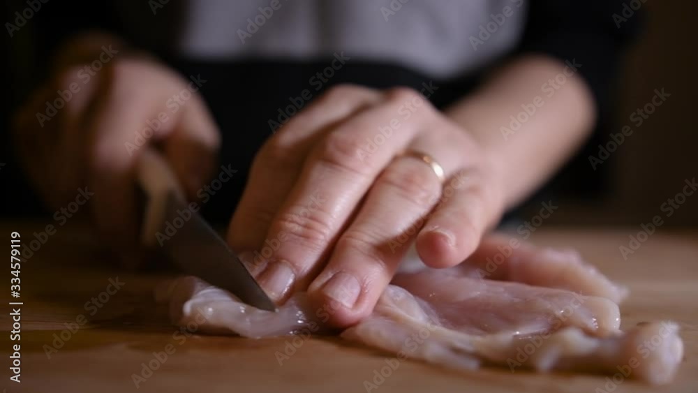 Caucasian woman cuts chicken breast on wooden cutting board in the kitchen Caucasian woman cuts chicken breast on wooden cutting board in the kitchen