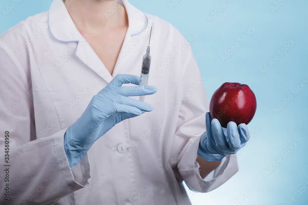 Portrait of a female doctor standing with an Apple and a syringe on a blue background as the idea of antibiotics in vegetables and fruits Portrait of a female doctor standing with an Apple and a syringe on a blue background as the idea of antibiotics in vegetables and fruits