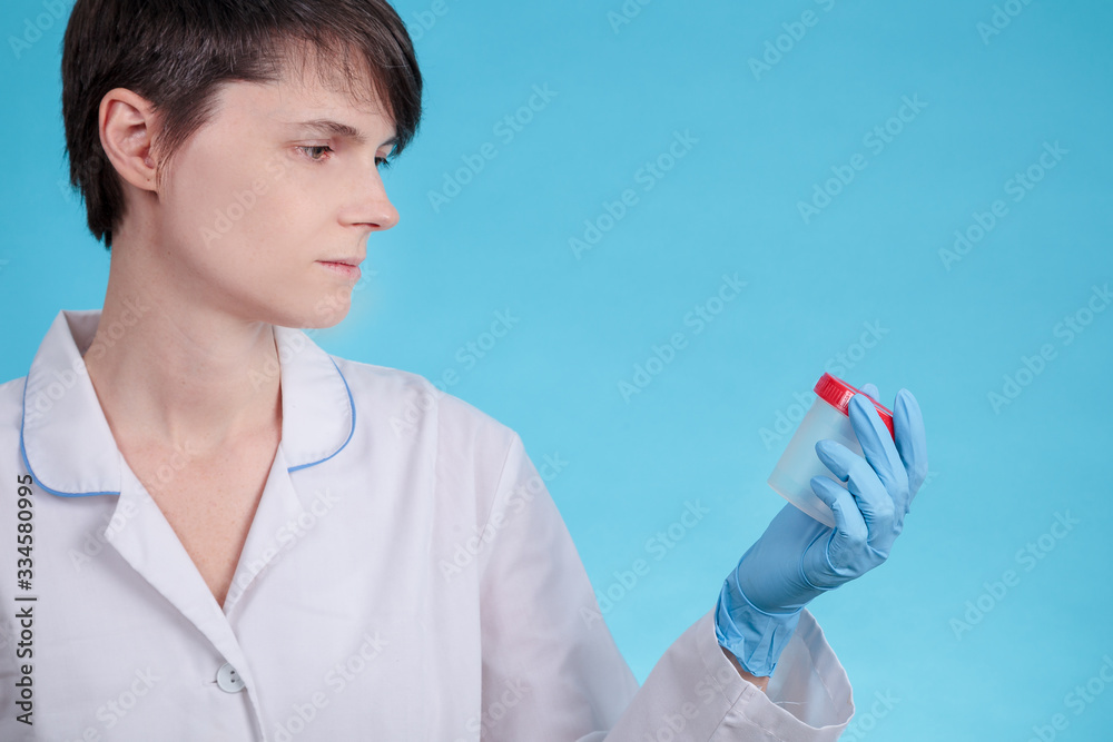doctor in a white uniform and blue gloves on a blue background holds an empty plastic test jar. drug test, virus, disease doctor in a white uniform and blue gloves on a blue background holds an empty plastic test jar. drug test, virus, disease