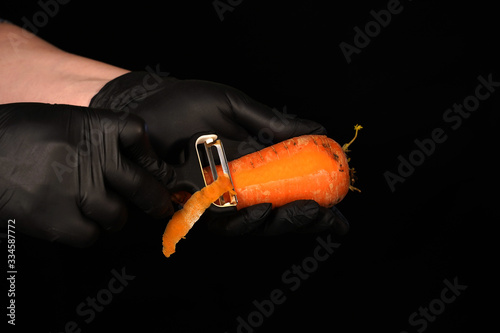 Peel the carrots with a special knife. Hands of assistant chef on dark background photo