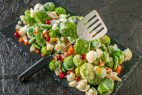 Set of frozen vegetables and fruits on a black kitchen board.