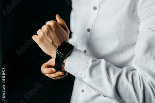 Men in white shirt puts on the watch on black background