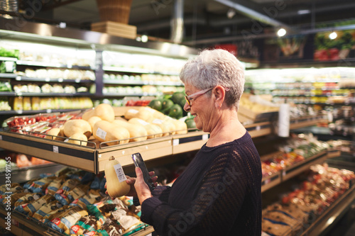 Senior woman with smart phone shopping in supermarket produce section photo