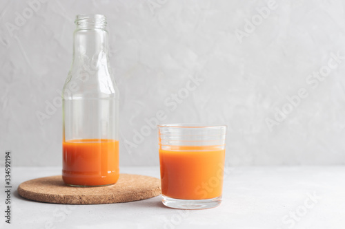 Glass bottle with carrot juice and a glass of juice stand next to a gray background. A healthy diet. Fresh Juice. Copy space