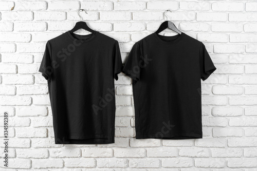 Black t-shirt hanging on a hanger against brick wall, front view