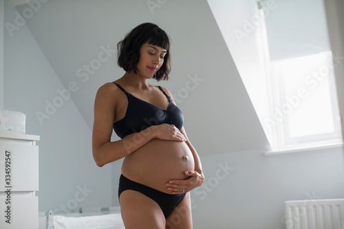 Serene pregnant woman in bra and panties holding stomach