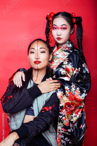 two pretty geisha girls friends: modern asian woman and traditional wearing kimono posing cheerful on red background © iordani