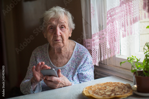 An elderly woman, old pensioner sits with a smartphone in her hands..