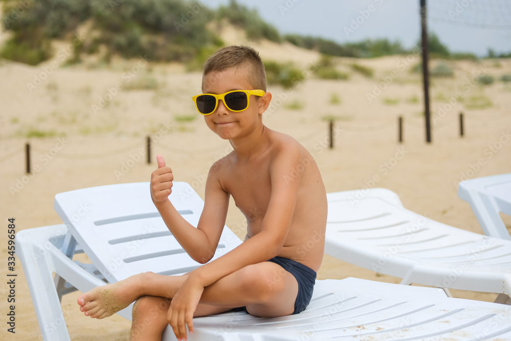 Modern young guy in sunglasses is sunbathing on a sunbed on the sea beach.