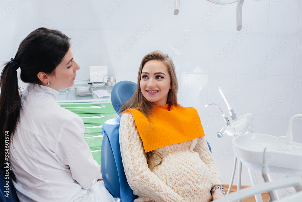 A professional dentist treats and examines the oral cavity of a pregnant girl in a modern dental office. Dentistry