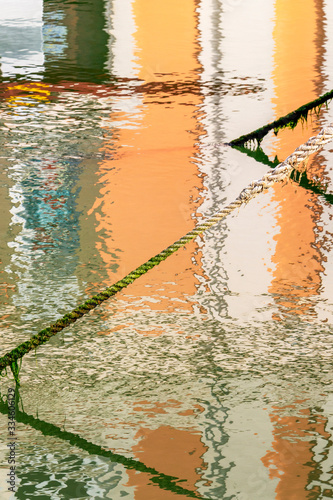 Fototapeta Naklejka Na Ścianę i Meble -  Weathered mooring line with algae on a blurred building distorted reflection in the water surface of Fosso Venarella canal or Leonardo's Port Canal at Cesenatico, Province of Forli-Cesena, Emilia-Roma
