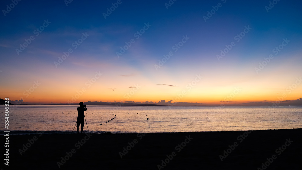 The silhouette of a photographer taking a photo of a beautiful sunset at tropical beach.