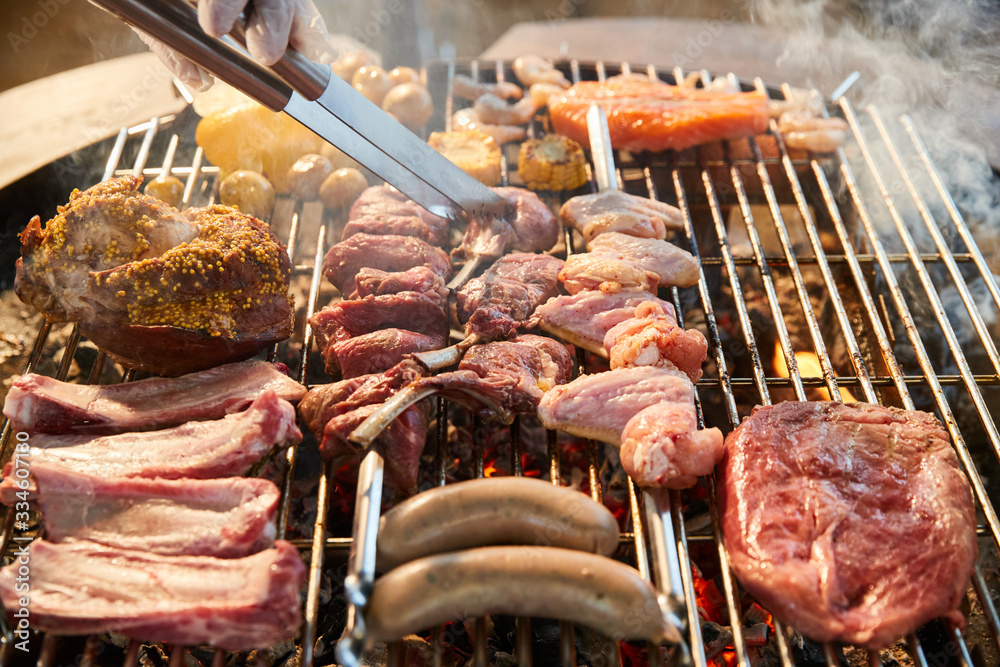 The meat is pickled on a lattice grill, ribs spread, a stake, Sausages, edges, chicken, naked flame, black pepper, a smoke, firewood, hands of the chef display meat, Hands in gloves, close up