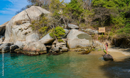 Young woman lifting her arms up, happy hispanic girl in caribbean beach with turquoise waters. Positive human emotion. Free happy girl enjoying nature. Tayrona National Park, Cabo San Juan, Colombia.