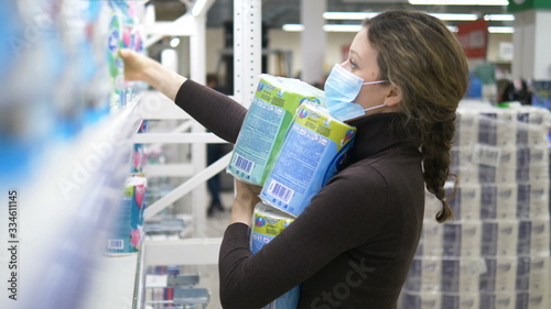 A young woman in a medical mask takes a lot of toilet paper in a supermarket photo