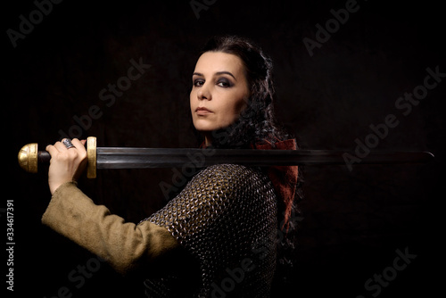 A dark-haired woman with a sword, a Scandinavian warrior in a chain mail against a dark background