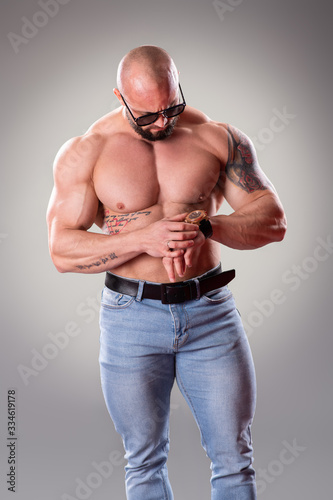 Sexy muscular bodybuider looking at his watch on the gray background photo