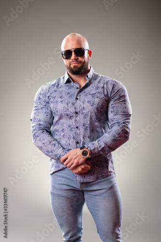 Sexy dressed muscular bodybuider with sunglasses on the gray background photo