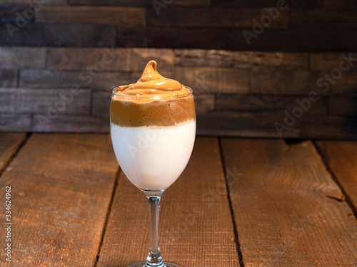 Whipped Dalgona coffee latte in a clear stem glass on a wooden background.