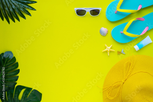 Summer holiday of traveler women. Top view from above of beach accessories and a hat with sunglasses and sandals on yellow background. Flat lay with copy space. Tropical fashion vacation concept.