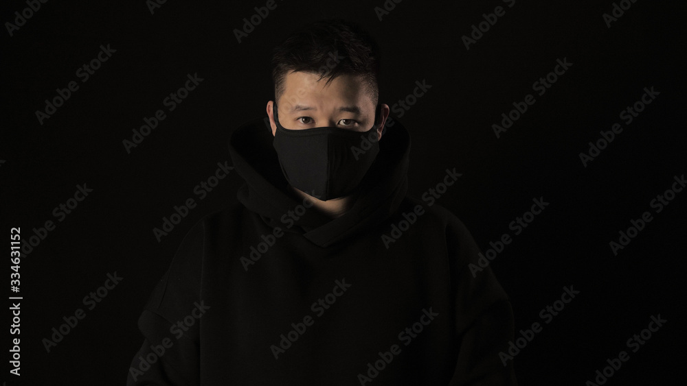 Asian man in a black medical mask from coronavirus on a black background with white tape covid 19 Asian man in a black medical mask from coronavirus on a black background with white tape covid 19