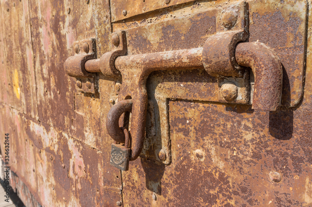 Old weathered bolt with lock on it and dated rusty factory gate in the background in the sunlight Old weathered bolt with lock on it and dated rusty factory gate in the background in the sunlight
