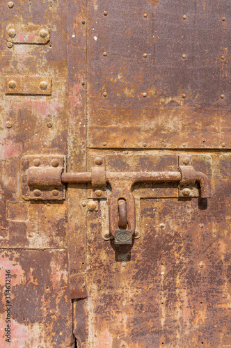 Old weathered bolt with lock on it and dated rusty factory gate in the background in the sunlight © Andy