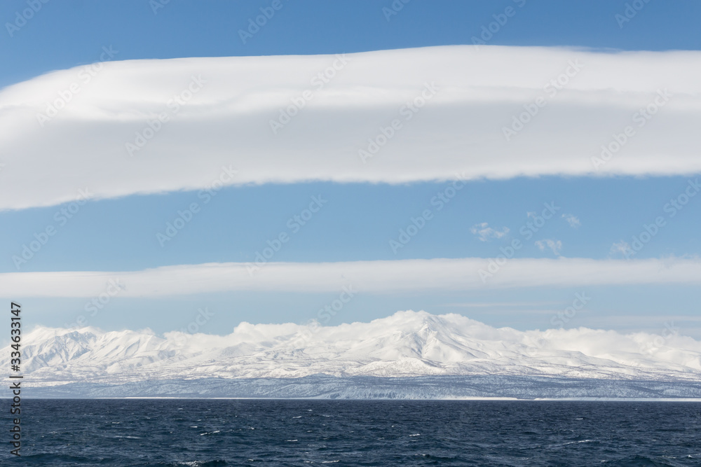 Seascape, dark sea, snowy mountains in the distance, a big white cloud