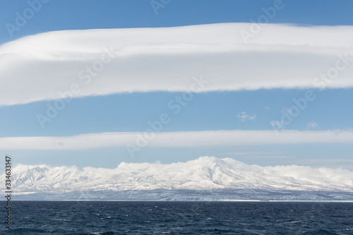 Seascape, dark sea, snowy mountains in the distance, a big white cloud