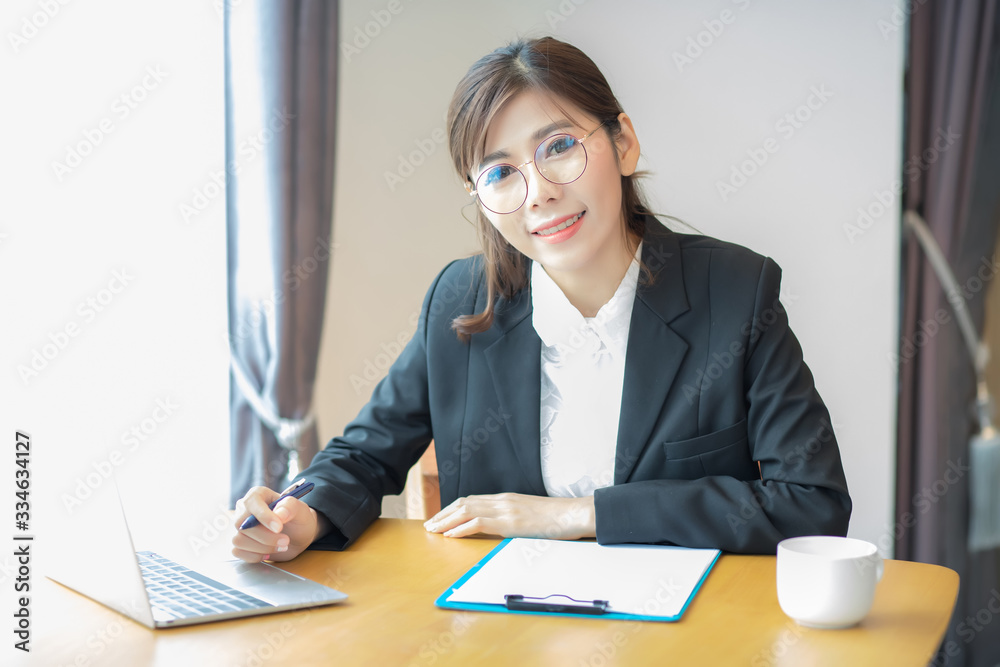 A beautiful Asian woman, Thai woman, is sitting at home after work is closed due to the effects of the corona virus or the covid-19 virus. On the table is a notebook computer laptop placed. A beautiful Asian woman, Thai woman, is sitting at home after work is closed due to the effects of the corona virus or the covid-19 virus. On the table is a notebook computer laptop placed.