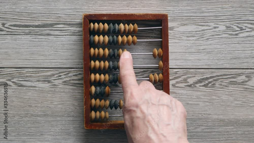 A Elderly Man Moves Wooden Knuckles On A Outdated Vintage Wooden Abacus On A Gray Desk, Close-up. . A Elderly Man Moves Wooden Knuckles On A Outdated Vintage Wooden Abacus On A Gray Desk, Close-up. .