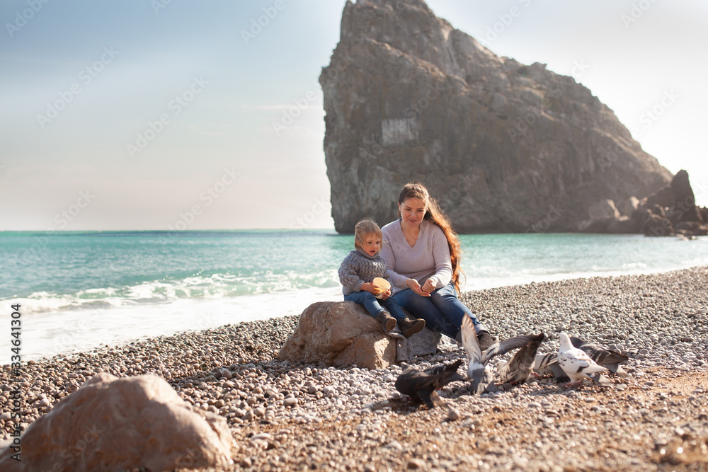 Happy pretty girl and mom walk along the sea coast against the background of the sea, from behind a beautiful landscape Happy pretty girl and mom walk along the sea coast against the background of the sea, from behind a beautiful landscape