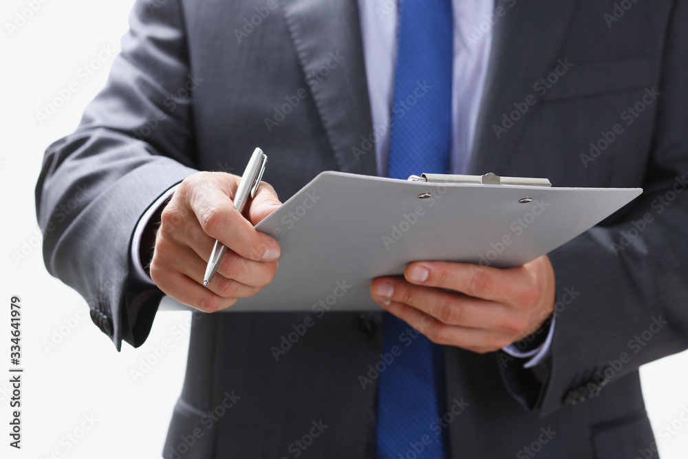 Hand of businessman in suit filling and signing with silver pen partnership agreement form clipped to pad closeup. Management training course some important document team leader ambition concept Hand of businessman in suit filling and signing with silver pen partnership agreement form clipped to pad closeup. Management training course some important document team leader ambition concept