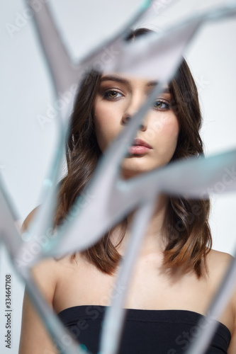 Young woman looks in a broken mirror. Portrait of beautiful female in the mirror shards