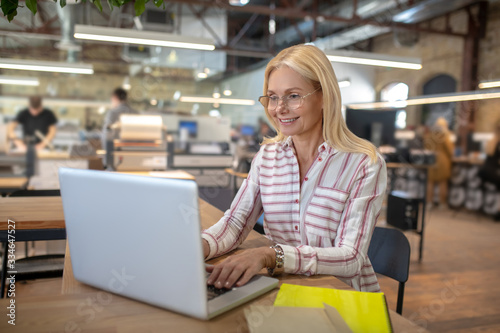 Blonde woman sitting in workshop  typing on laptop
