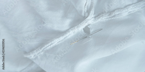 Mending clothes. Repairing fabric, shopping less concept. White dress with hole, thread and needle. Stock photo.